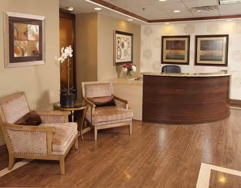 Reception area in a Grove of Elmhurst senior living lobby with wood desk, chairs, and art.