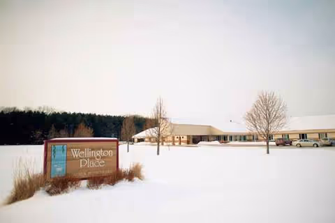 Snow-covered front yard with Wellington Place sign and building in the distance.