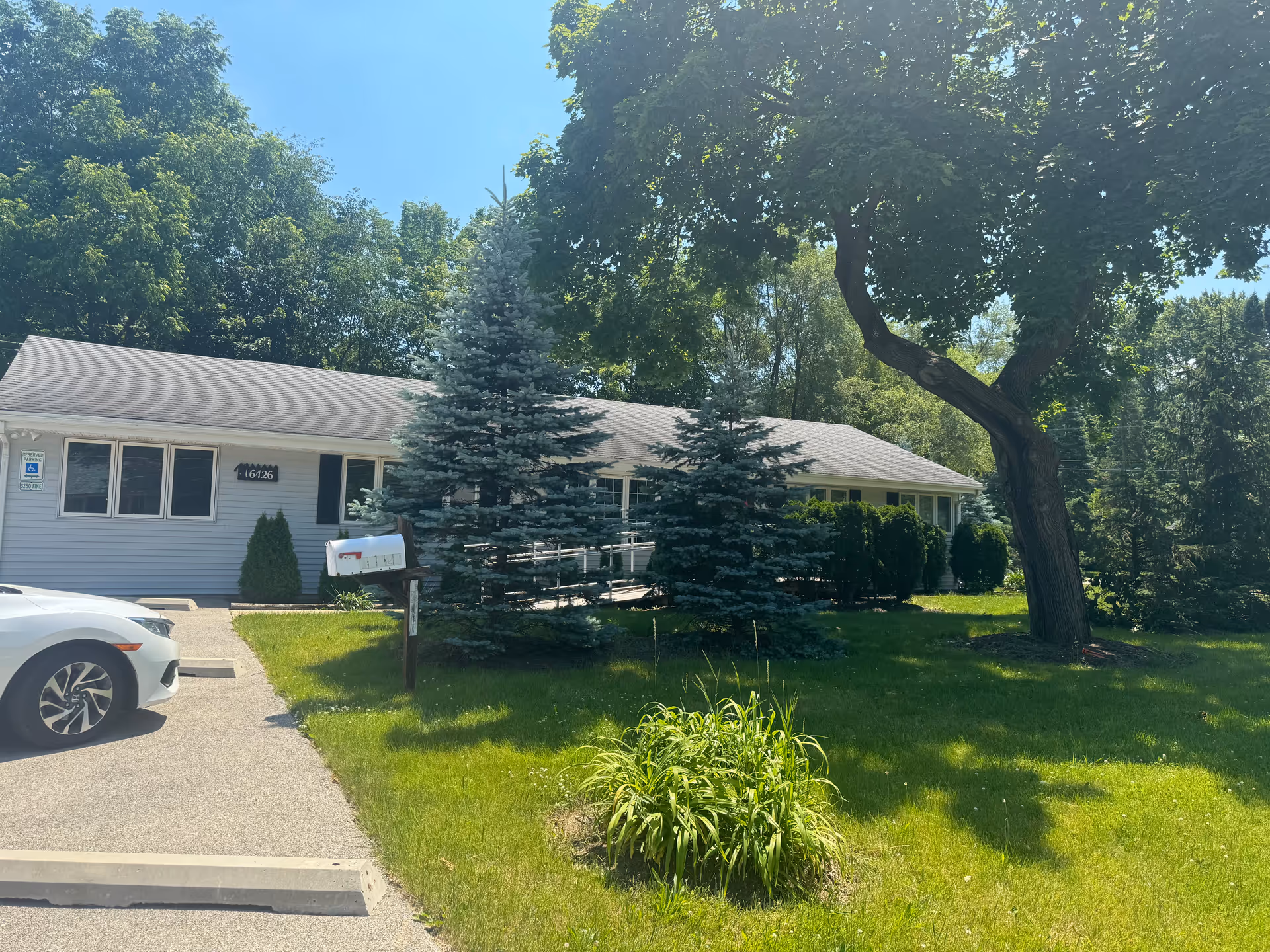 Front view of Theresa's Home Care 4 facility, with a lawn, trees, and parked car.