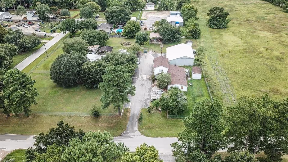 Aerial view of a senior living facility named Down Home Blessed Care showing several buildings surrounded by trees, grassy areas, and a few parked cars. The facility is located along a road with open fields and residential houses nearby.