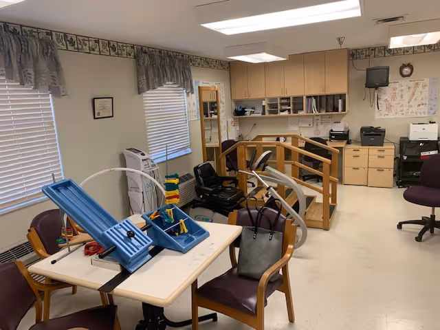 Interior therapy/activity room with a table and chairs, exercise equipment, and a small practice staircase with handrails.