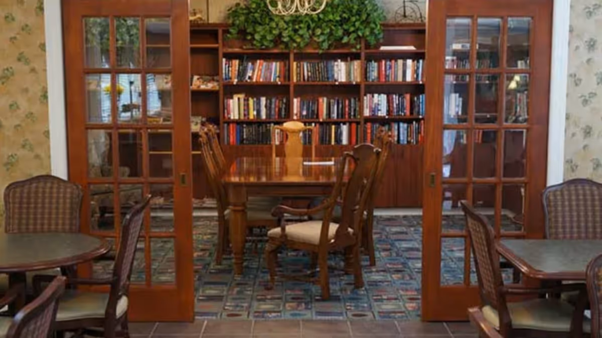 Glass-paneled double doors open onto a room with a wooden dining table and chairs in front of a wall of bookshelves.