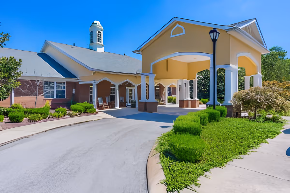 Exterior view of Charter Senior Living of Hermitage showing the entrance with a covered driveway, manicured bushes, and a clear blue sky.