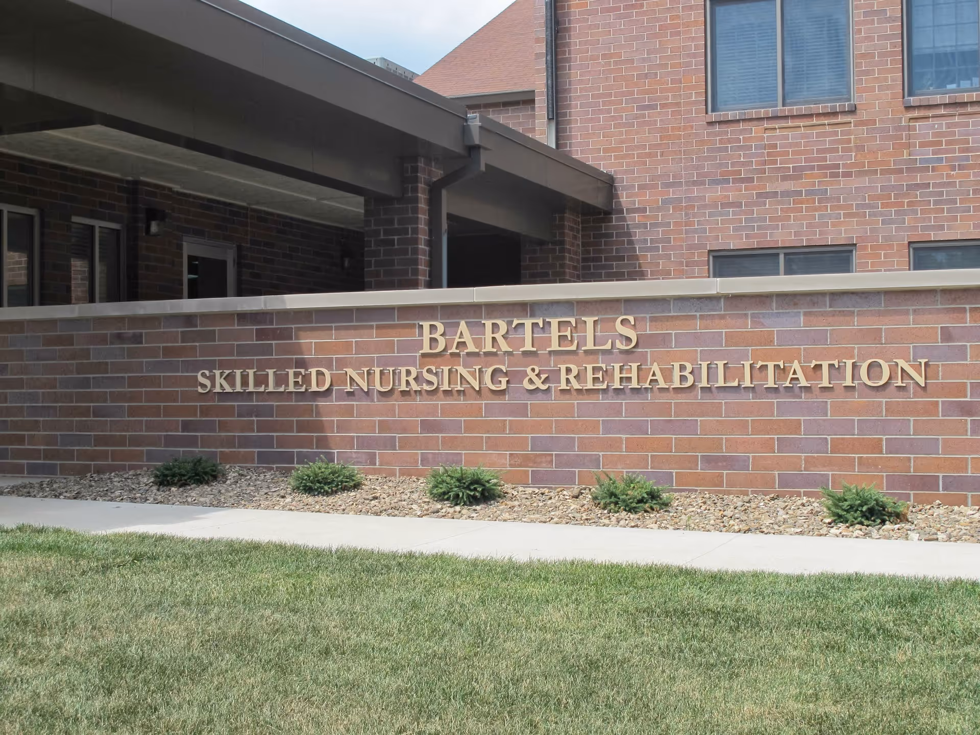 Front exterior of a brick building with a sign reading 'BARTELS SKILLED NURSING & REHABILITATION' above a landscaped lawn.