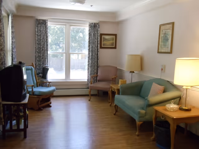 A bright living room with a couch, armchairs, side tables and a TV facing a large window.