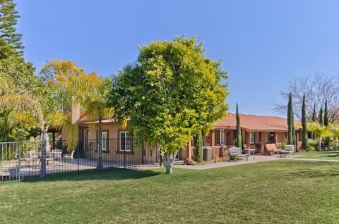 Single-story building with a red-tiled roof surrounded by green grass, trees, and outdoor seating under a clear blue sky at Hilltop Country Estate.