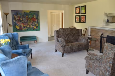Cozy living room with upholstered seating, fireplace, artwork, and a doorway in background.