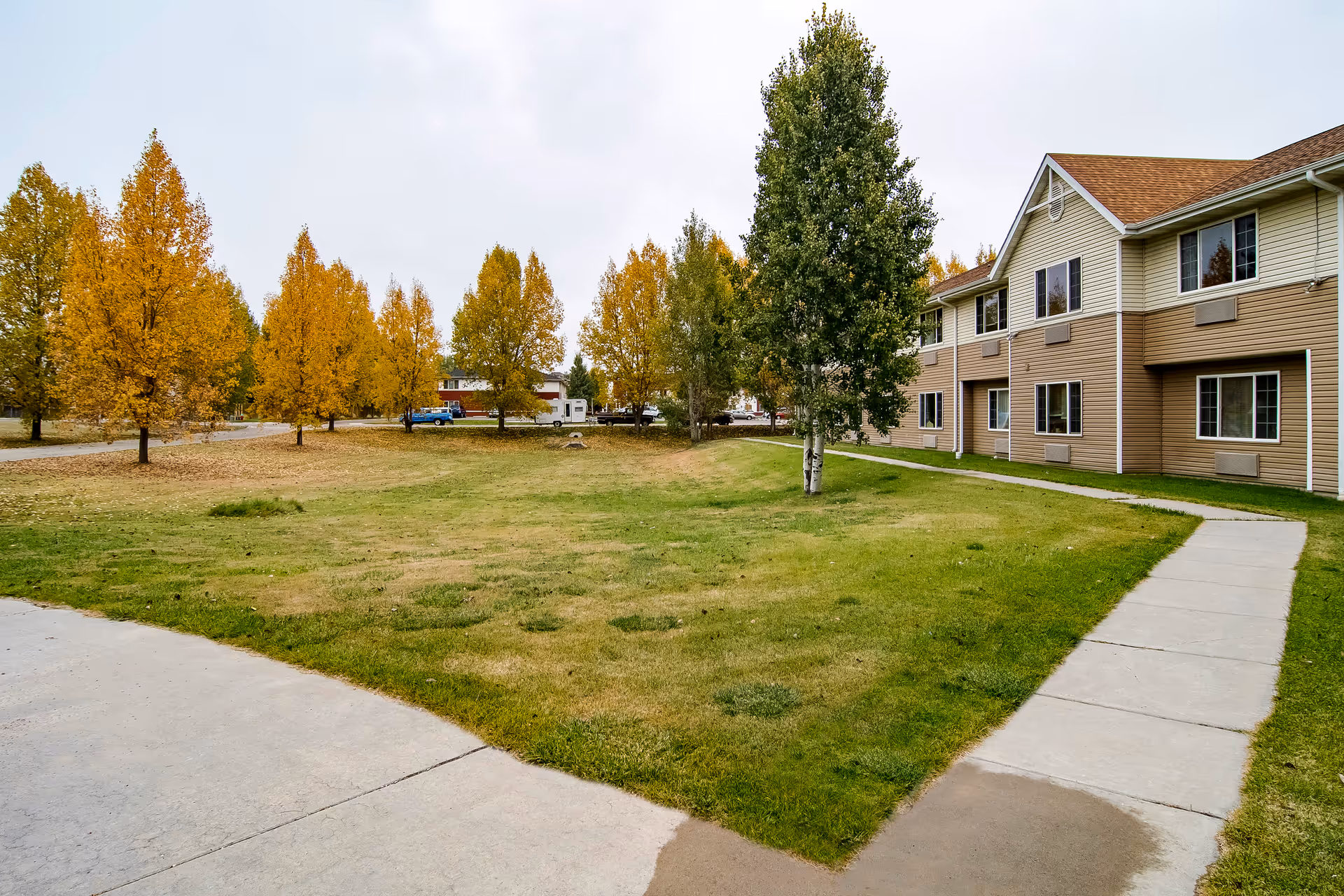Outdoor view of a senior living facility named Edgewood Sierra Hills showing a grassy lawn with a concrete walkway, several trees with autumn foliage, and a two-story building with beige siding and multiple windows.