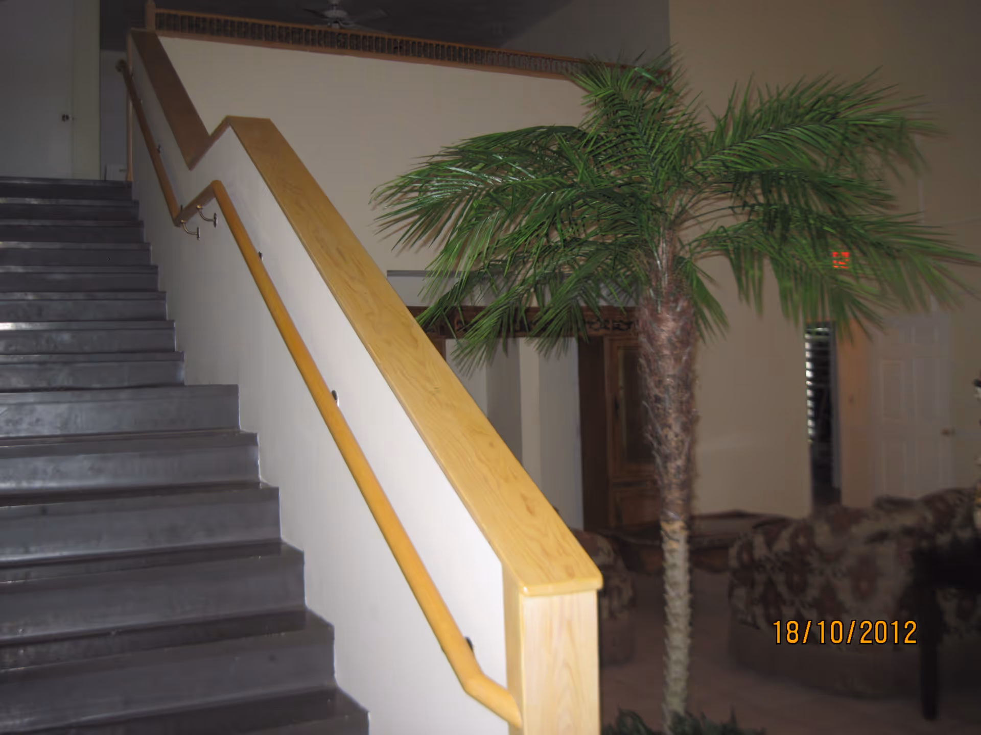 Interior view showing a stairway with a wooden handrail, an indoor palm tree, and a seating area.