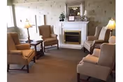 Upholstered wingback chairs arranged around a fireplace with a mantel mirror, side tables, and lamps in a cozy sitting room.