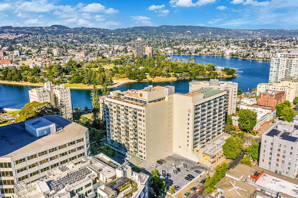 Aerial view of a large multi-story residential building beside a lake with surrounding cityscape and parkland.