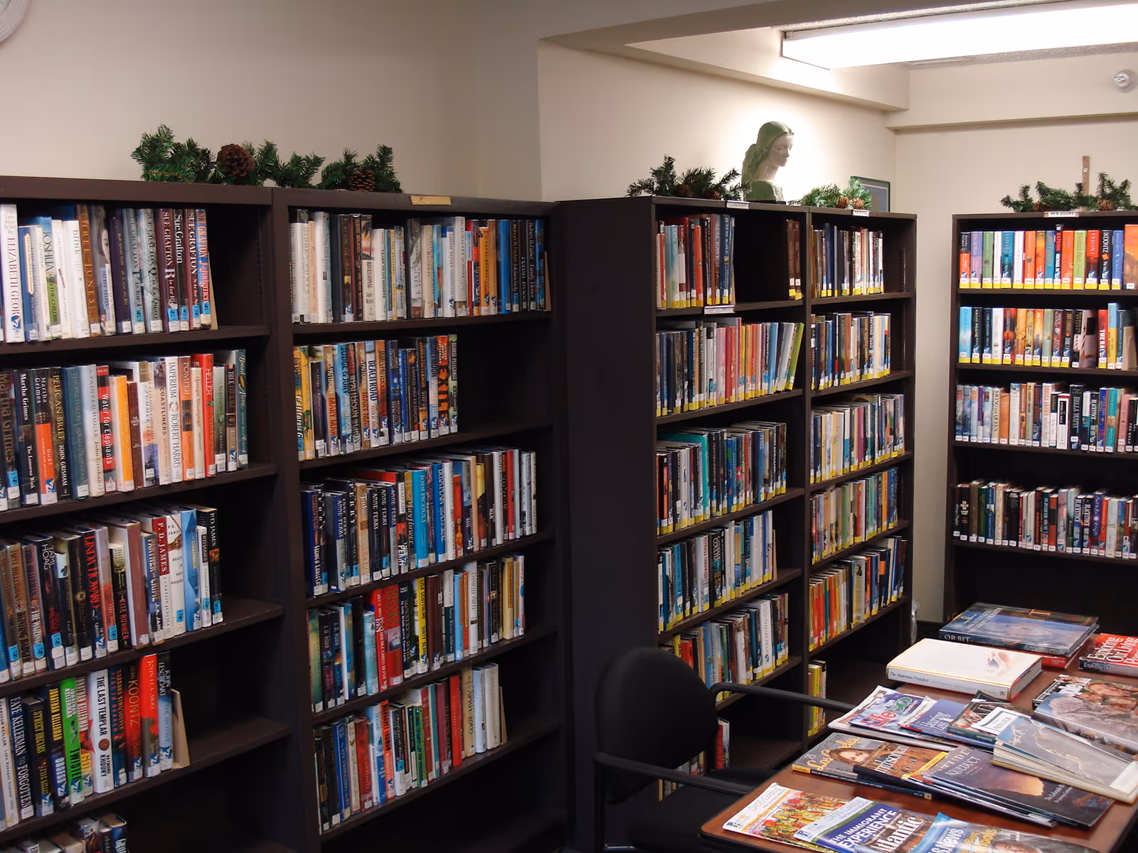 A small interior library with tall dark bookshelves filled with books and a table covered in magazines.
