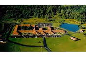 Aerial view of Rolling Fields Eldercare Community showing a large building complex with red roofs surrounded by green lawns and trees, with a pond on the right side and a small pavilion near the pond.