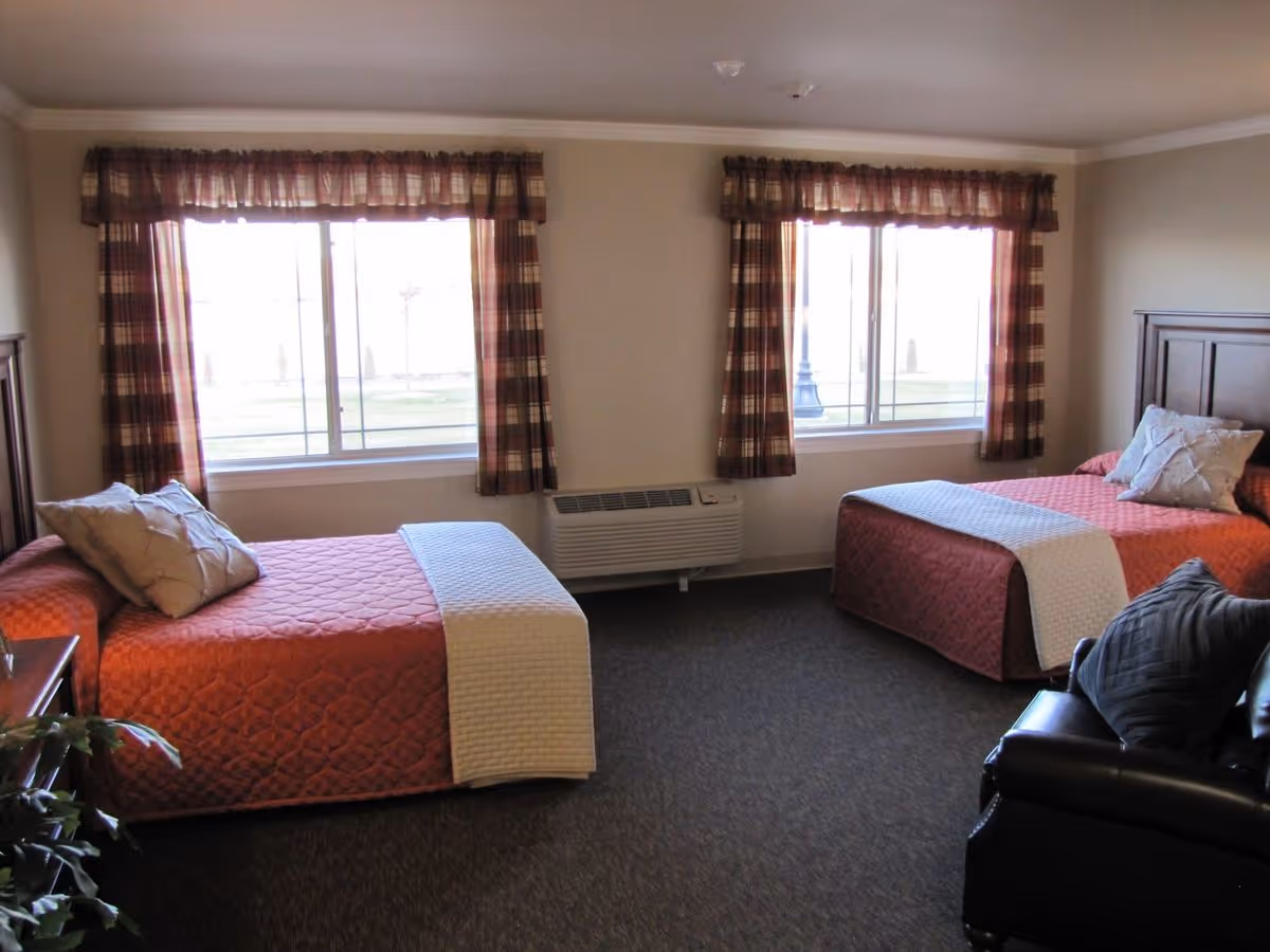 Two-bed bedroom with plaid-curtained windows, matching orange bedspreads, and a chair.