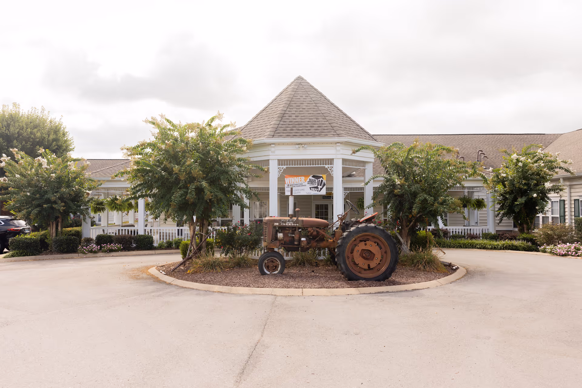 Front entrance of a senior living building with a circular driveway and an old tractor displayed on the center island.