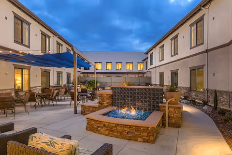 Outdoor courtyard at dusk featuring a central stone fire pit, patio seating, and a two-story surrounding building.