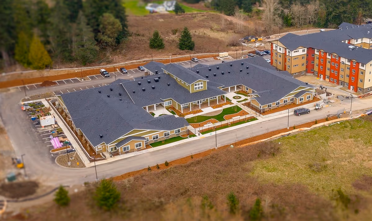 Aerial exterior view of a single-story memory care facility with central courtyards, parking areas, and neighboring buildings.