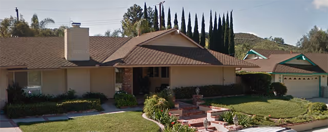 Front view of a single-story ranch-style assisted living building with a tiled roof, brick entry steps, manicured lawn, and attached garage.