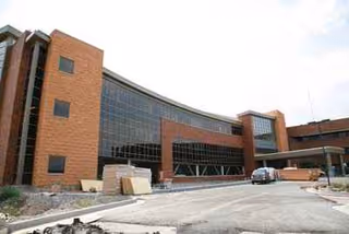 Exterior view of a brick and glass hospital building with a curved entrance and parking.