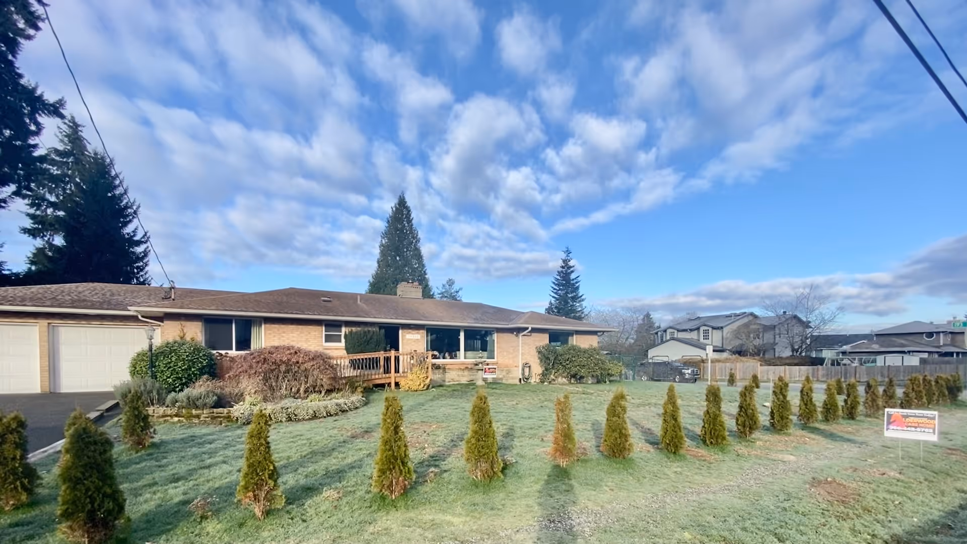A residential facility with a front lawn, trees, and blue sky.