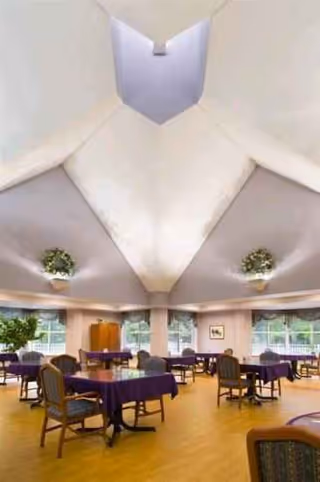A bright dining area with round tables, purple tablecloths, and potted plants.