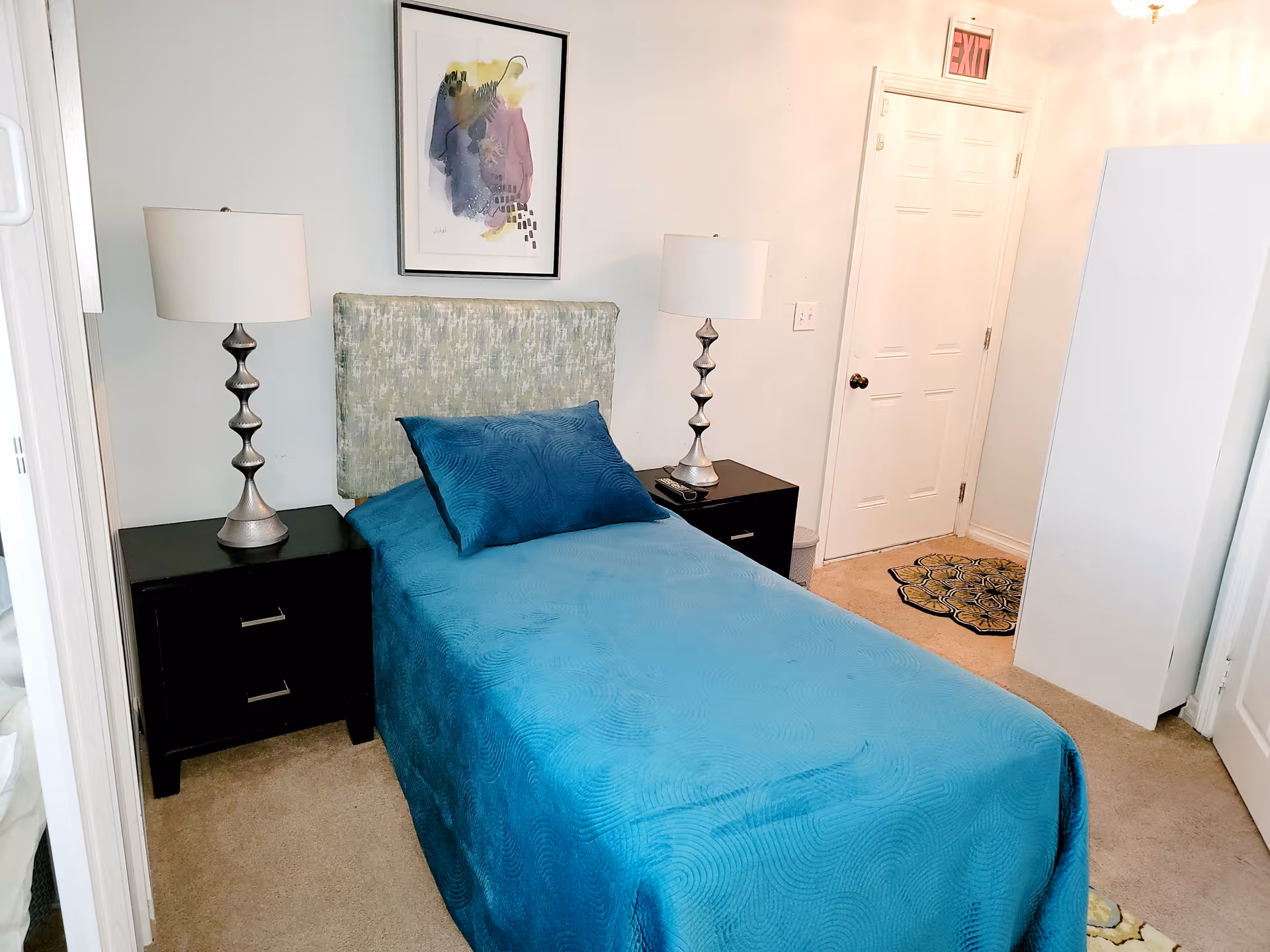 A blue-covered single bed with two nightstands, lamps, and wall art in a bedroom.