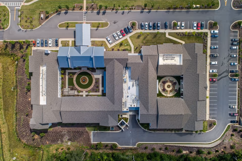 Aerial view of a large U-shaped senior living facility with two central courtyards, surrounding parking lots and driveways.
