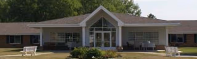Front view of a single-story senior living facility with glass entry and outdoor seating.