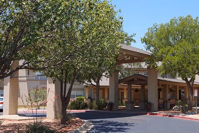 Covered entrance and porte-cochère of a senior living building with trees and a driveway.