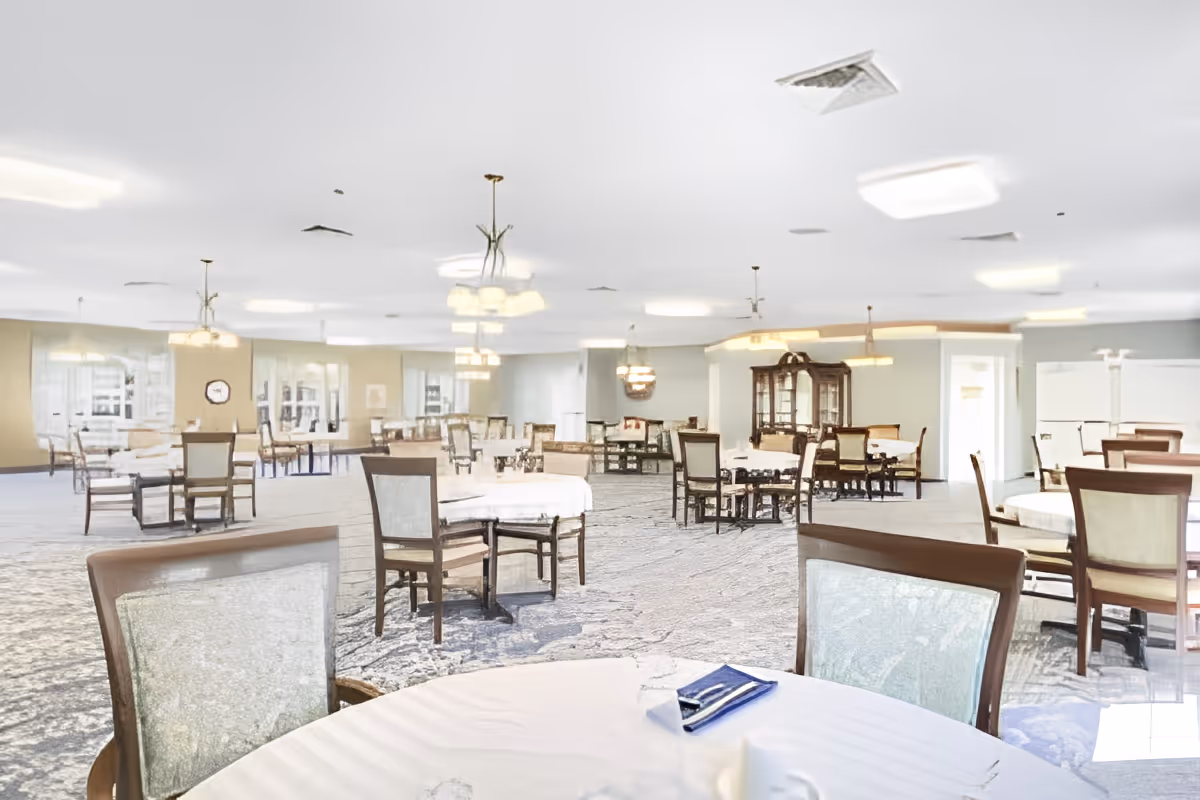 Bright, spacious dining room with round tables, upholstered chairs, and chandeliers.
