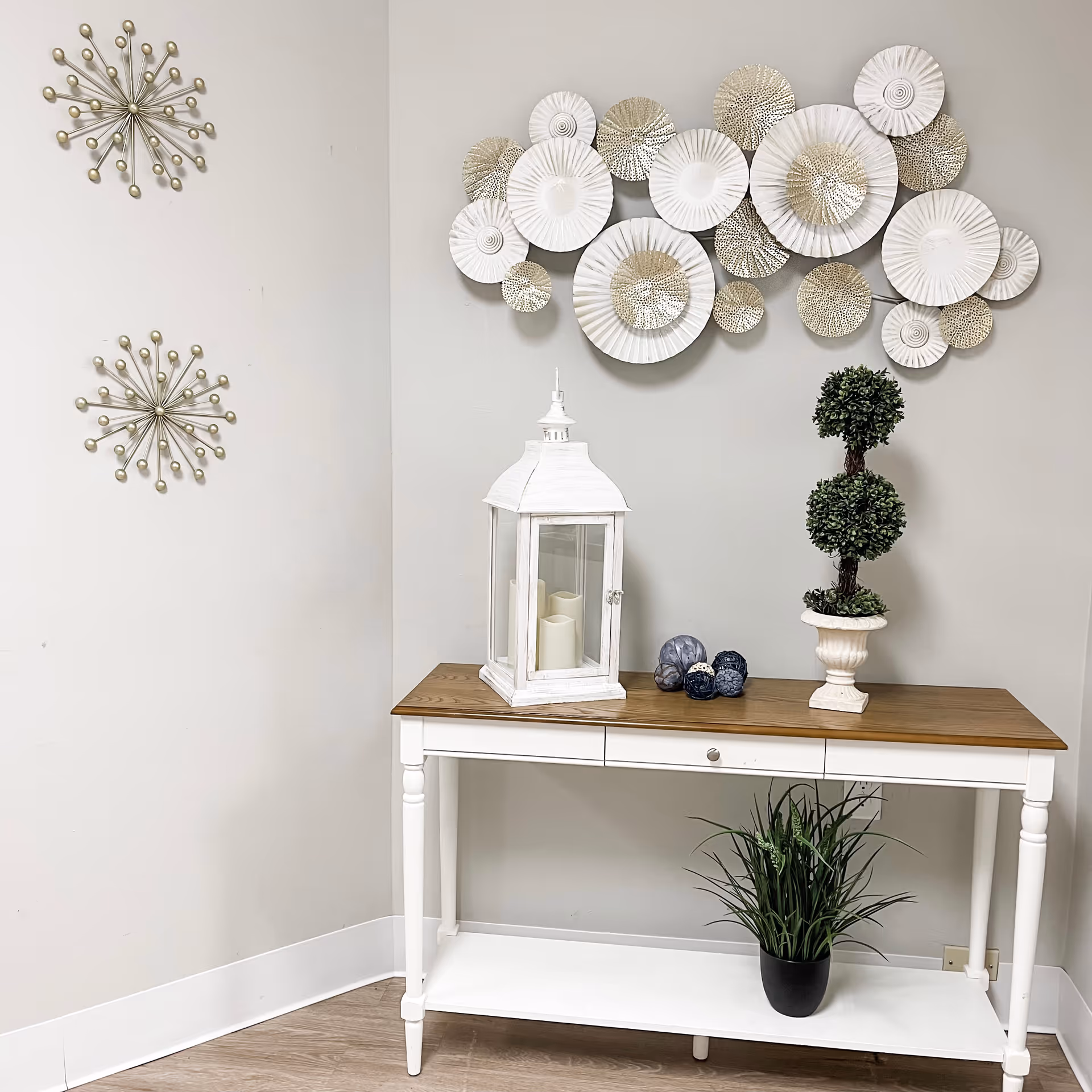 White console table with a lantern, potted topiary and decorative objects beneath a wall of circular metal art.
