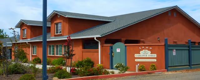Red stucco building with a green gated entrance, landscaped front, and a sign reading 'Larkspur Lodge'.