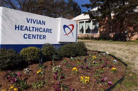 A Vivian Healthcare Center sign in front of a brick building with a flower bed.
