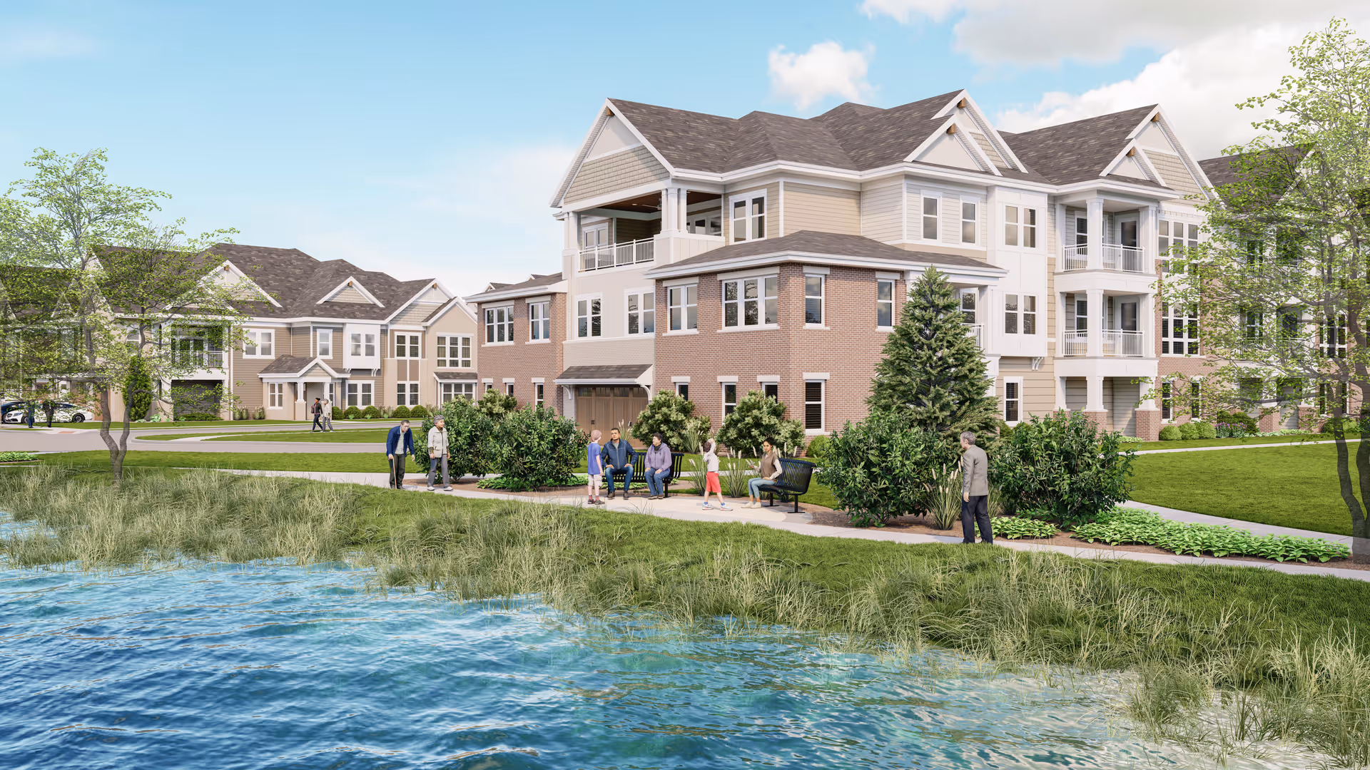 Exterior view of a senior living facility named Greenwood Village South, showing multi-story residential buildings with balconies and large windows. There is a pond in the foreground with grassy banks, a walking path alongside it, and several people walking or sitting on benches. Trees and shrubs are planted around the buildings and along the path under a partly cloudy sky.