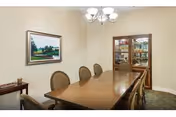 Formal dining room featuring a long wooden table surrounded by upholstered chairs, a chandelier, framed landscape painting, and a glass-front china cabinet.