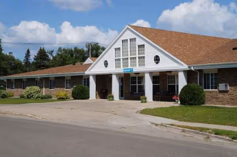 Single-story brick senior living facility with a covered entrance and neatly trimmed shrubs.