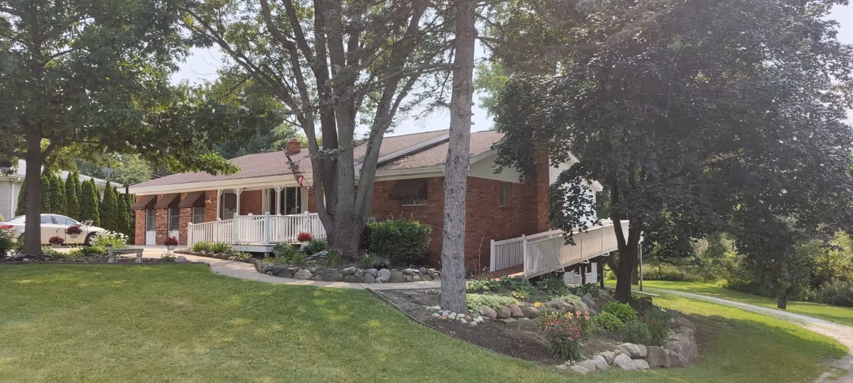 Brick ranch-style building with a covered front porch, wheelchair ramp, landscaped lawn and large trees.