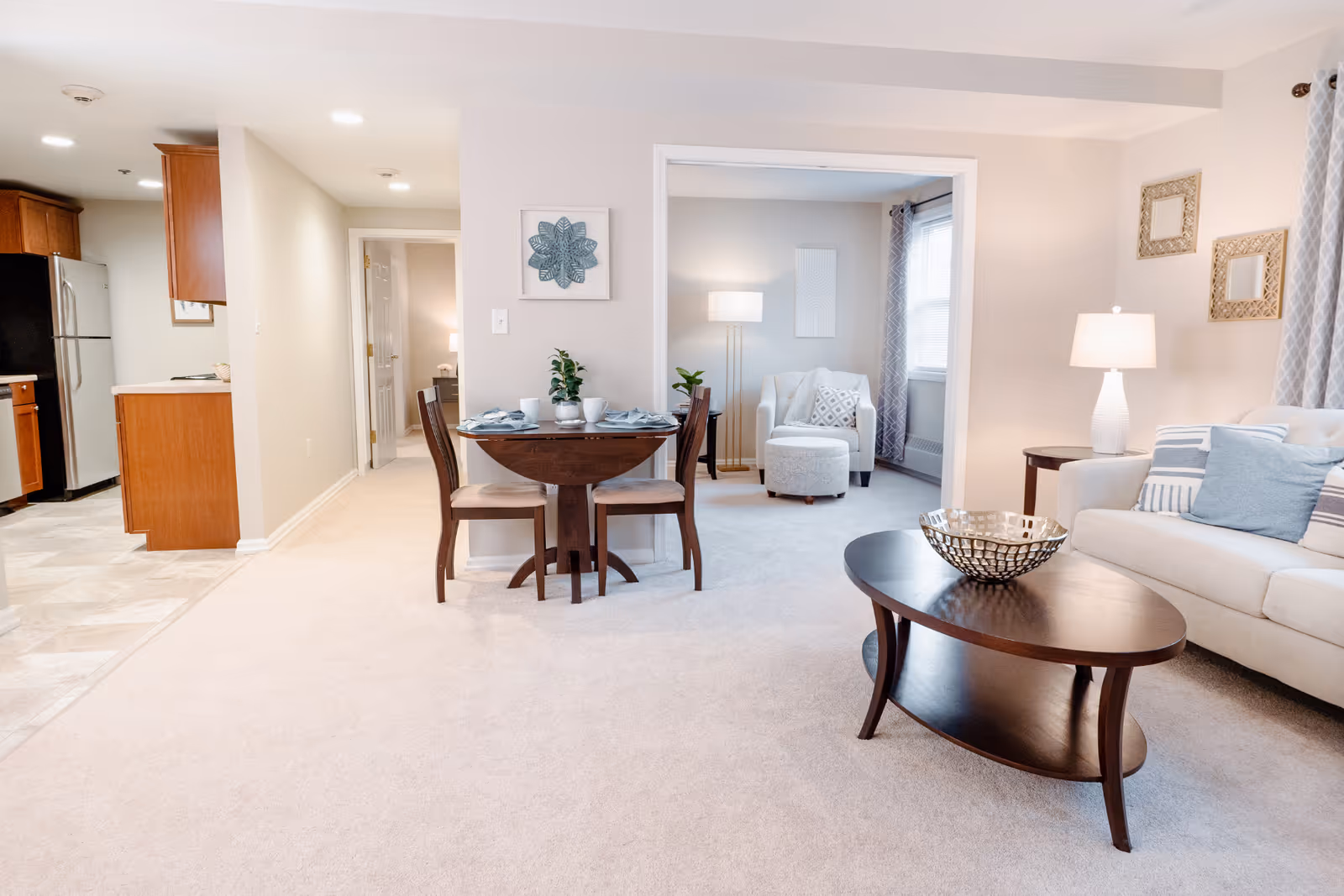 Bright open living and dining area with a sofa, coffee table, small round dining table, and an adjacent kitchen.