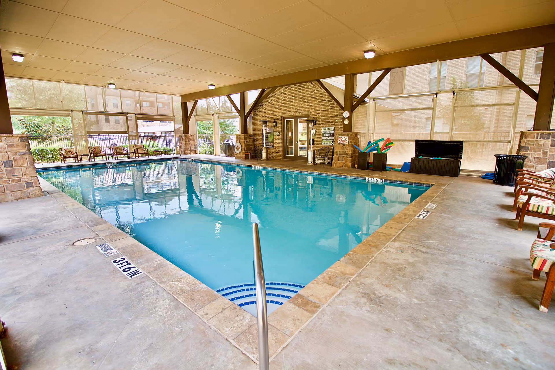 Covered indoor swimming pool with lounge chairs and pool equipment inside a senior living facility.