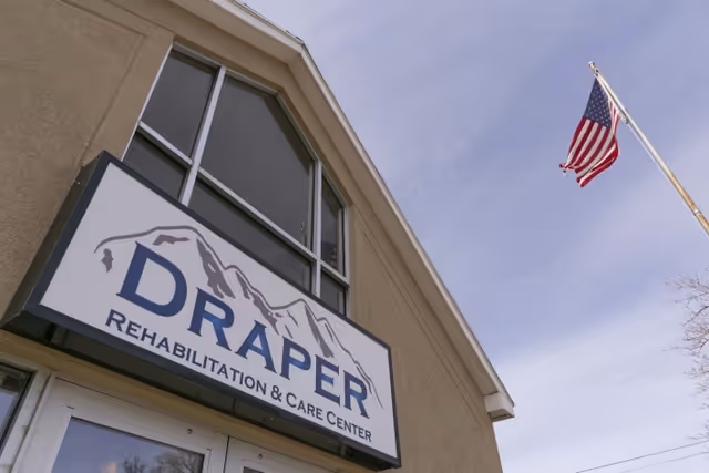 Exterior view of the Draper Rehabilitation & Care Center sign on the building with an American flag flying nearby.