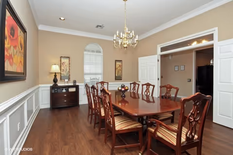 Formal dining room with a long polished wooden table, eight chairs, chandelier, sideboard, wall art, and hardwood floors.