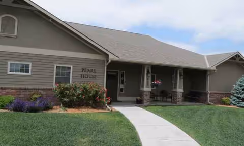 Front view of Pearl House senior living facility with walkway, lawn, and shaded porch.