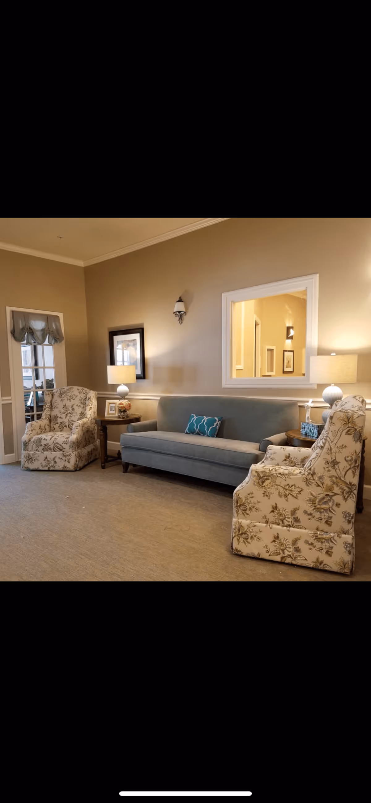 Neutral-toned lounge with a blue sofa, two floral armchairs, side tables with lamps and framed wall decor.