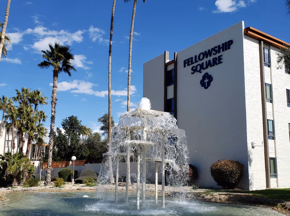 White Fellowship Square building with a water fountain, palm trees, and blue sky.