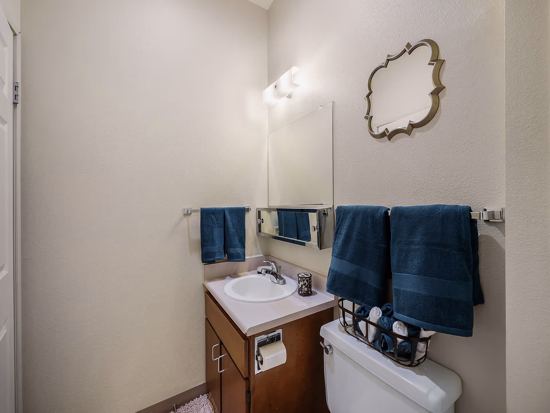 Small bathroom with a sink vanity, mirror, toilet, and blue towels hanging on racks.