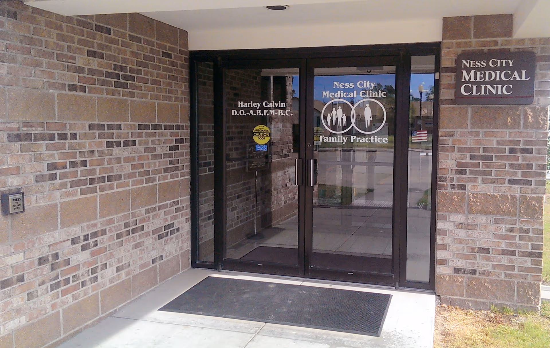 Glass double-door entrance to Ness City Medical Clinic set in a brick exterior with a sign on the wall.