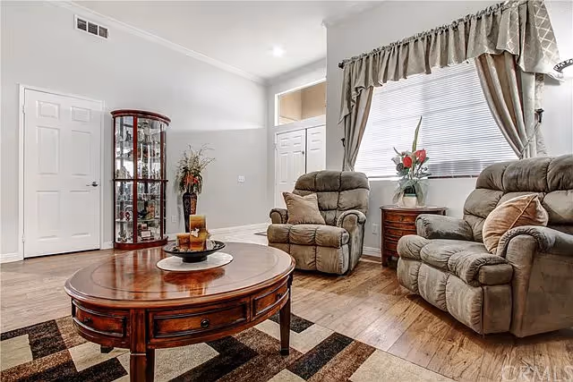 Bright living room with two recliner chairs, a wooden coffee table, a display cabinet, and a window with curtains.