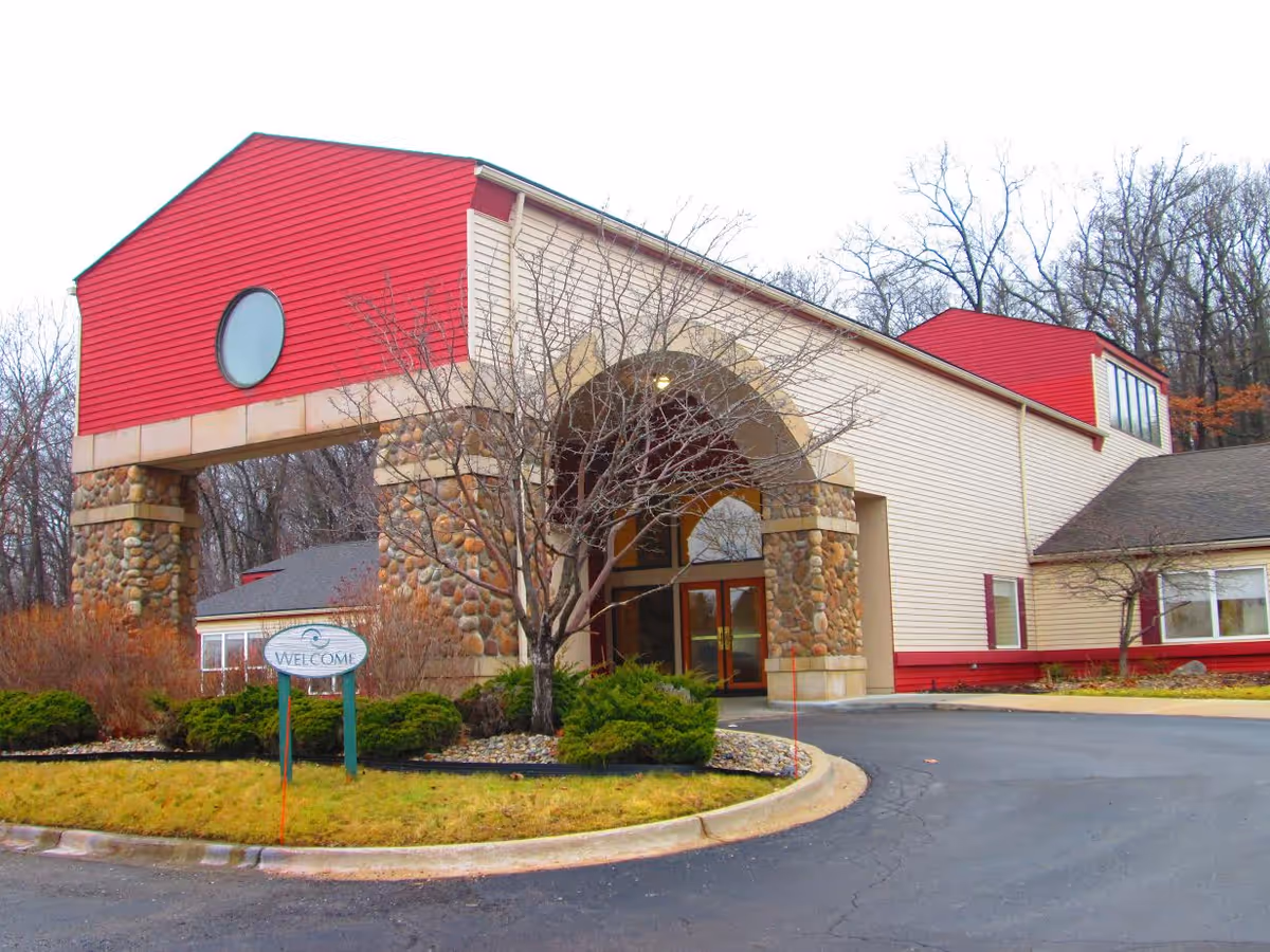 Exterior view of Medilodge of Milford showing the front entrance with stone arches and red accents.