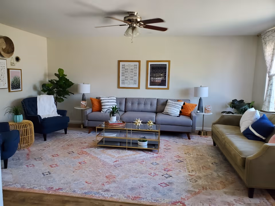 Bright, well-decorated living room with a gray sofa, armchairs, coffee table, rug and wall art.