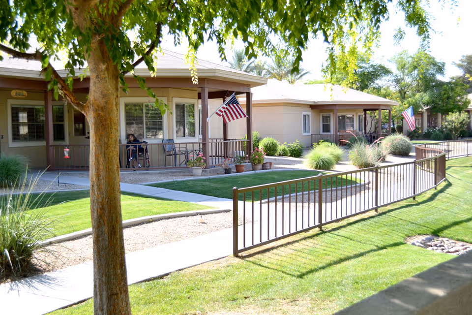 Exterior view of single-story senior living cottages with porches, American flags, walkways, and landscaped lawns.